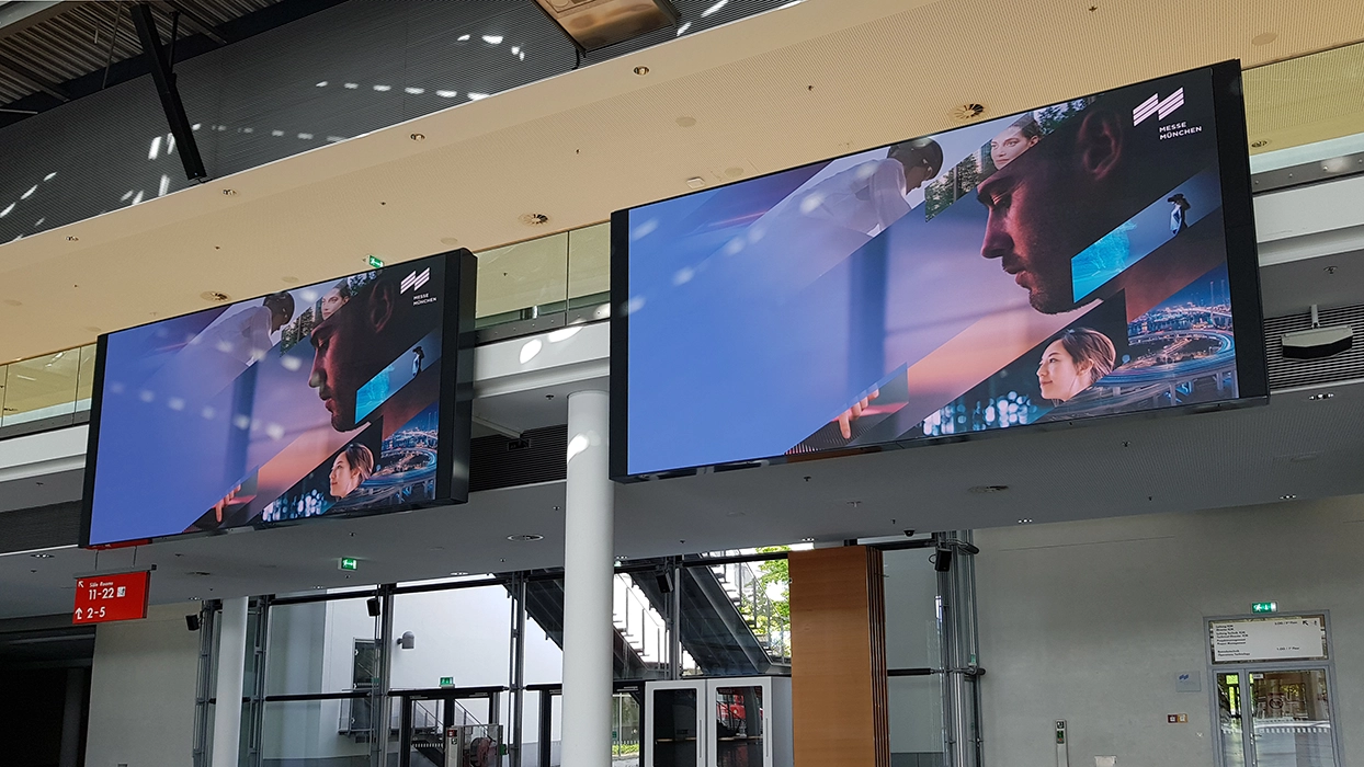 Two large television screens hang in a building.